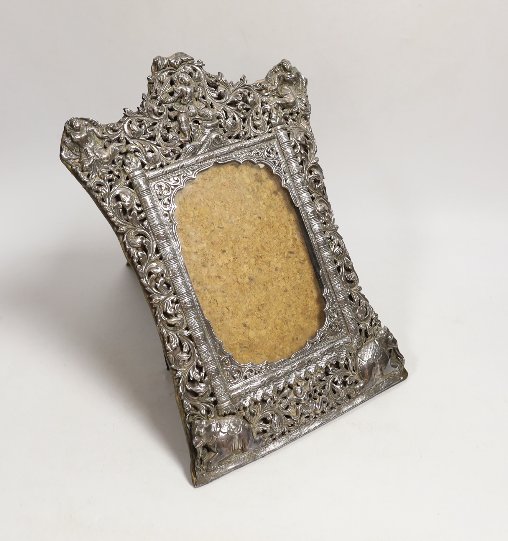 A Burmese white metal mounted shaped rectangular photograph frame, decorated with elephants and figures amongst scrolls, 29.2cm.